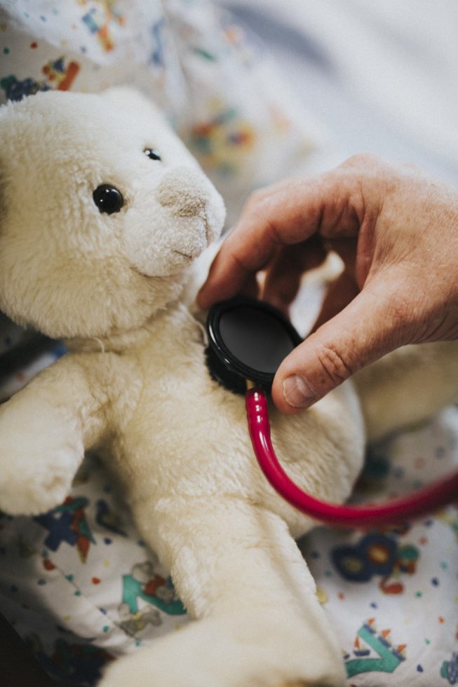 Doctor playfully checking the heart beat of a teddy bear